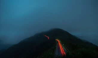 A glowing fog light cutting through mist on a winding mountain road at night.