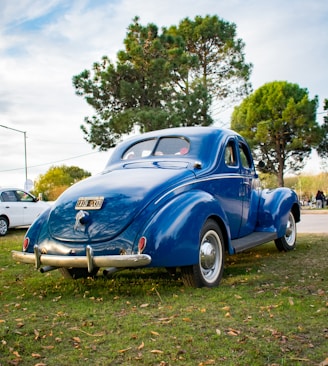 an old blue car parked in the grass