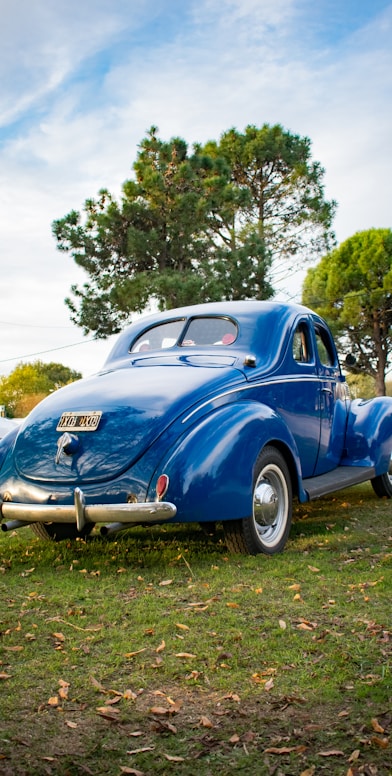 an old blue car parked in the grass