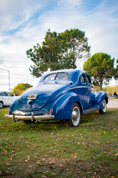 an old blue car parked in the grass