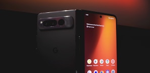 A smartphone with a foldable screen is partially unfolded, displaying its home screen with various app icons such as Keep Notes, Play Store, and Photos. The design is sleek, with a dark, reflective back and a prominent camera module. The lighting highlights the glossy surface, creating a modern and sophisticated look.