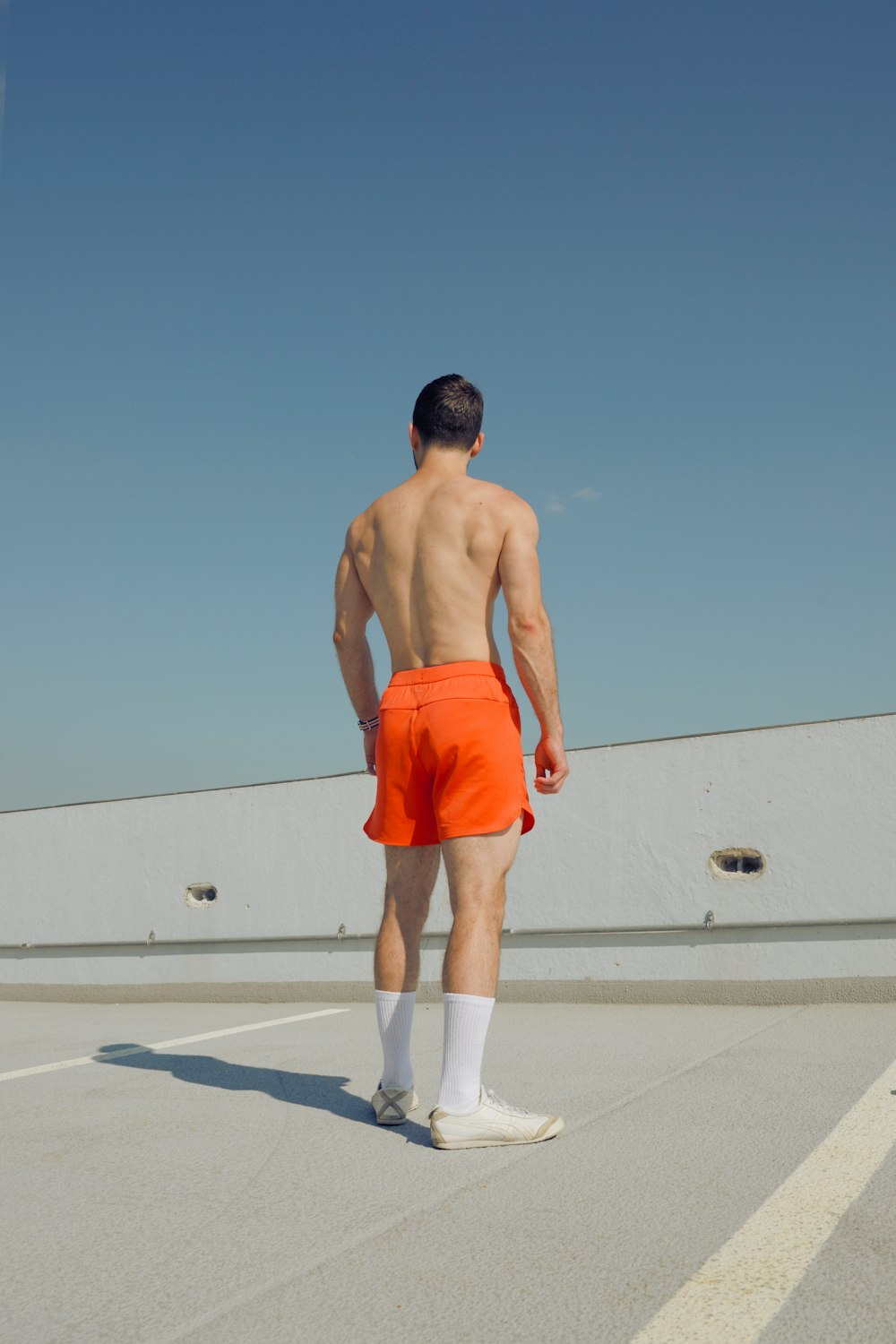 a shirtless man in an orange shorts is standing in a parking lot