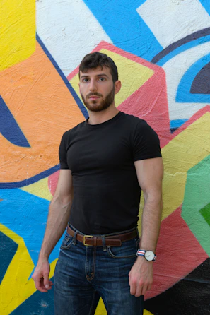 A close-up of a man wearing a bold graphic tee from threadvibe, standing against a city wall.