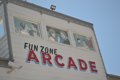 A white building with three windows displaying painted figures of people in conversation or interaction. The side of the building features the words 'FUN ZONE ARCADE' in bold, colorful letters.