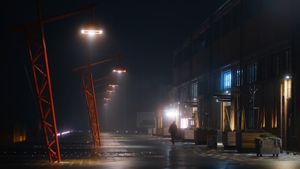 a dimply lit industrial area with a figure walking down a street