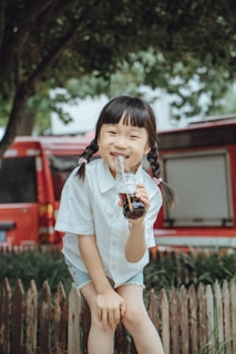 A smiling child holding a water bottle in an outdoor setting.