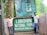 Two men standing next to the entrance sign of Lawachara National Park in Moulvibazar, Bangladesh. The area is lush with greenery and the sign is prominently displayed with informational boards above it.