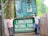 Two men standing next to the entrance sign of Lawachara National Park in Moulvibazar, Bangladesh. The area is lush with greenery and the sign is prominently displayed with informational boards above it.