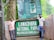 Two men standing next to the entrance sign of Lawachara National Park in Moulvibazar, Bangladesh. The area is lush with greenery and the sign is prominently displayed with informational boards above it.