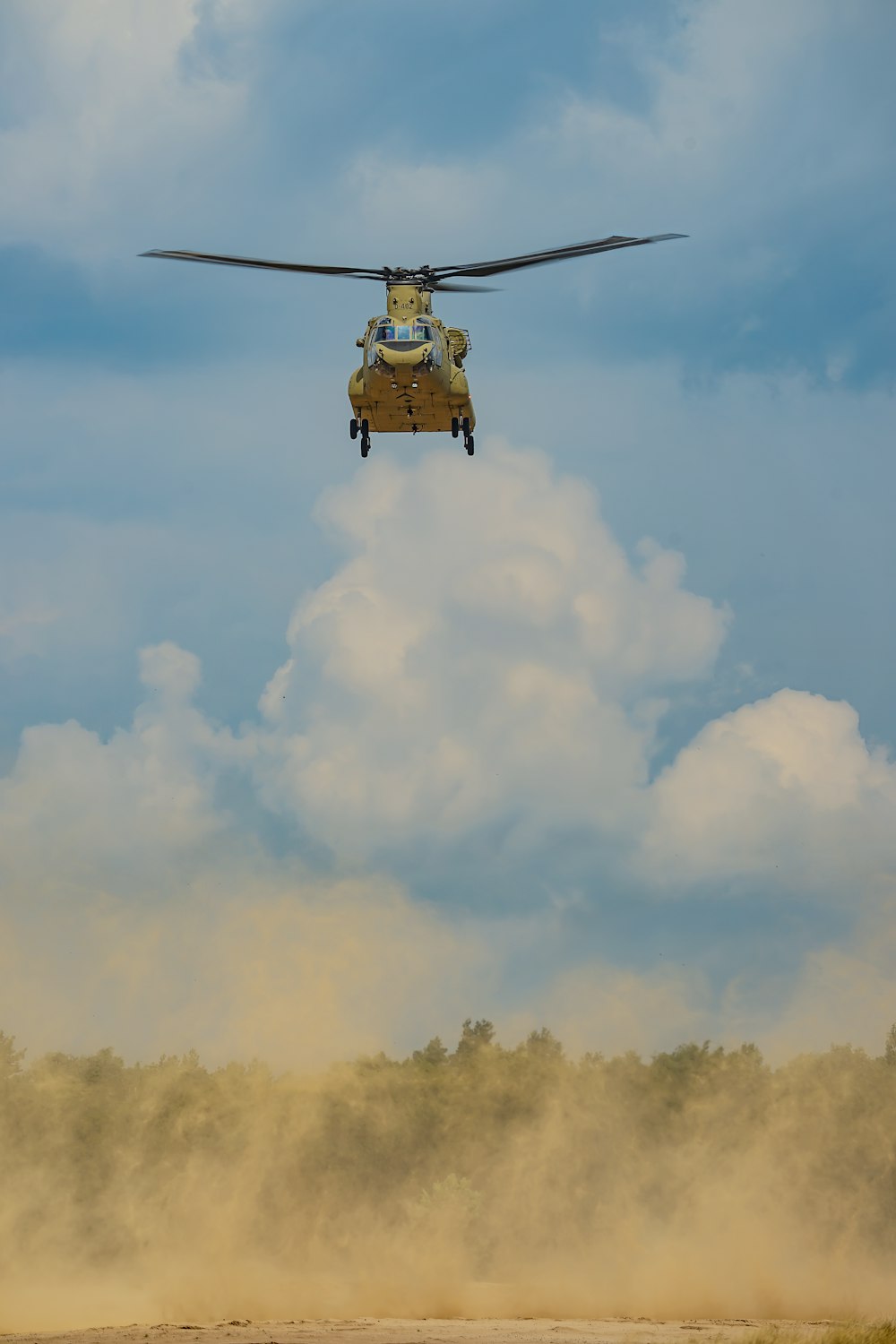 a helicopter flying over a dirt field under a cloudy blue sky