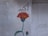 A simple wall mural featuring a red flower with yellow accents and a green stem, accompanied by Arabic script in black. The background is an uneven, light-colored surface that appears weathered.