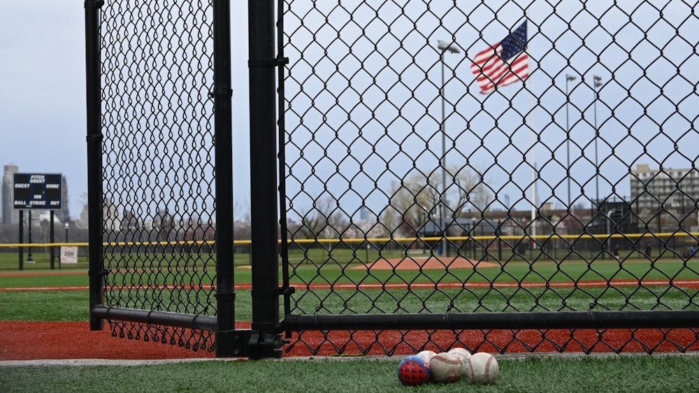 a baseball field with a fence and american flag in the background