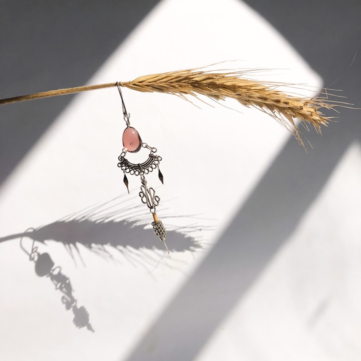 Close-up of delicate handmade fabric earrings in soft rose pink and gold tones on a white background