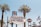 A vintage-style welcome sign displaying 'Welcome to Fabulous Las Vegas, Nevada' is surrounded by tall palm trees under a clear blue sky. An American flag waves on the right side, and a Harley-Davidson sign is visible in the background.