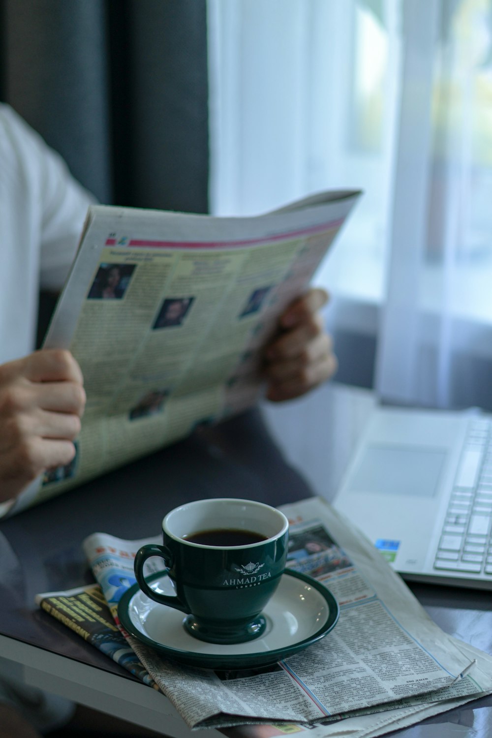 a person sitting at a table reading a newspaper and drinking a cup of coffee