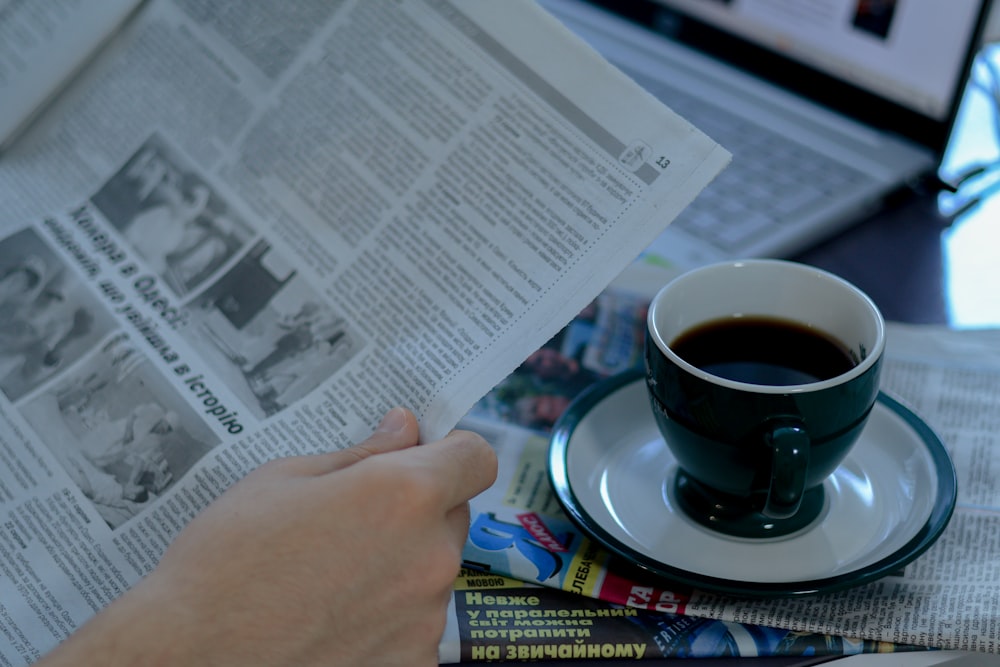 uma pessoa lendo um jornal com uma xícara de café