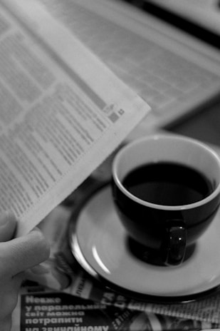 A close-up of a newspaper with Arabic headlines and a cup of coffee nearby.