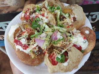A plate of Indian street food, specifically pani puri or golgappa, filled with vibrant ingredients. The round, crispy puris are topped with a mix of yogurt, tamarind chutney, finely chopped onions, fresh coriander, and crispy sev. Bright colors and a variety of textures are prominent.