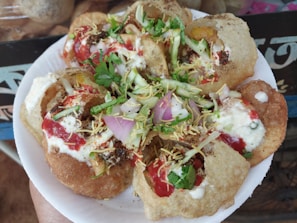 A plate of Indian street food, specifically pani puri or golgappa, filled with vibrant ingredients. The round, crispy puris are topped with a mix of yogurt, tamarind chutney, finely chopped onions, fresh coriander, and crispy sev. Bright colors and a variety of textures are prominent.