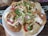 A plate of Indian street food, specifically pani puri or golgappa, filled with vibrant ingredients. The round, crispy puris are topped with a mix of yogurt, tamarind chutney, finely chopped onions, fresh coriander, and crispy sev. Bright colors and a variety of textures are prominent.