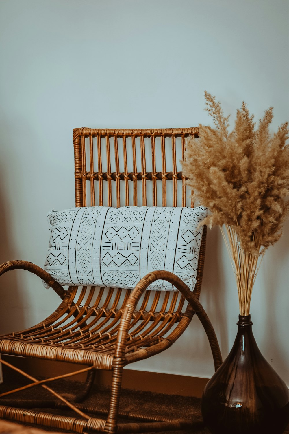 a wicker chair next to a vase with a plant in it