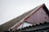 A close-up view of a sloped roof on a building, featuring corrugated material and a worn red wooden gable. Two metal bars with hooks are leaning against the roof. The sky is overcast, adding to the rustic and aged appearance of the scene.