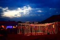 A nighttime community event illuminated by string lights, with people chatting and laughing.