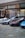 Several luxury sports cars are parked in front of a showroom with large glass windows. There are people standing near the entrance, possibly security or staff, and a striking art installation is visible above one of the cars.