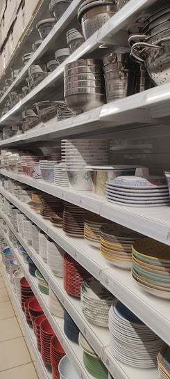 Shelves filled with a variety of kitchenware, including metal colanders, bowls, and stacks of ceramic plates in different colors and patterns.