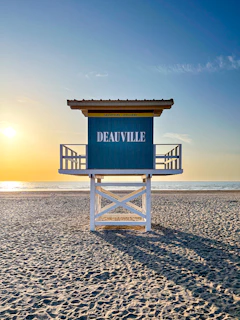 a lifeguard tower on a beach with the sun setting in the background