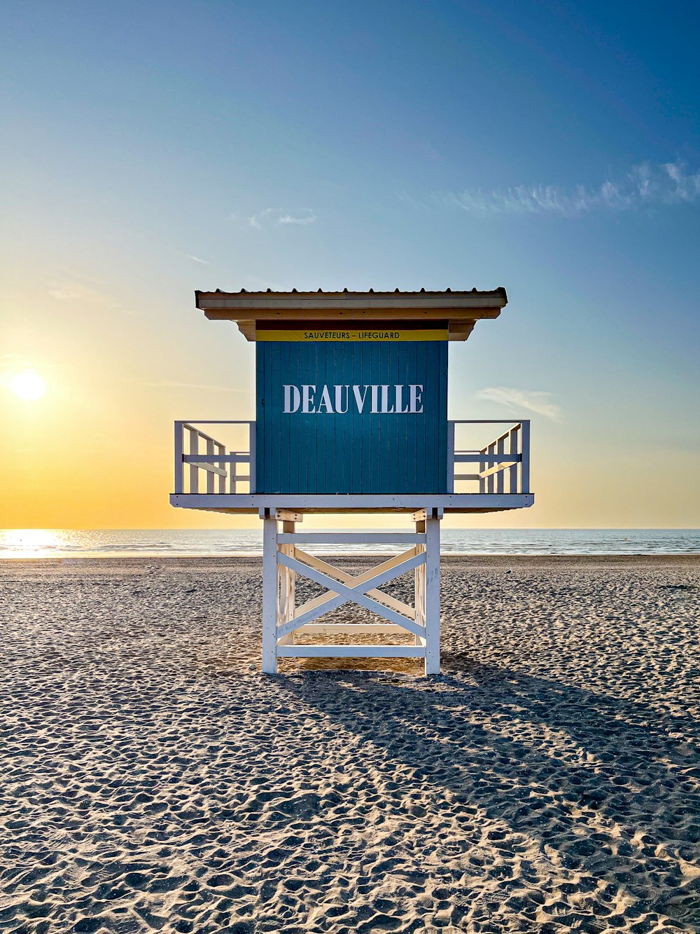 a lifeguard tower on a beach with the sun setting in the background