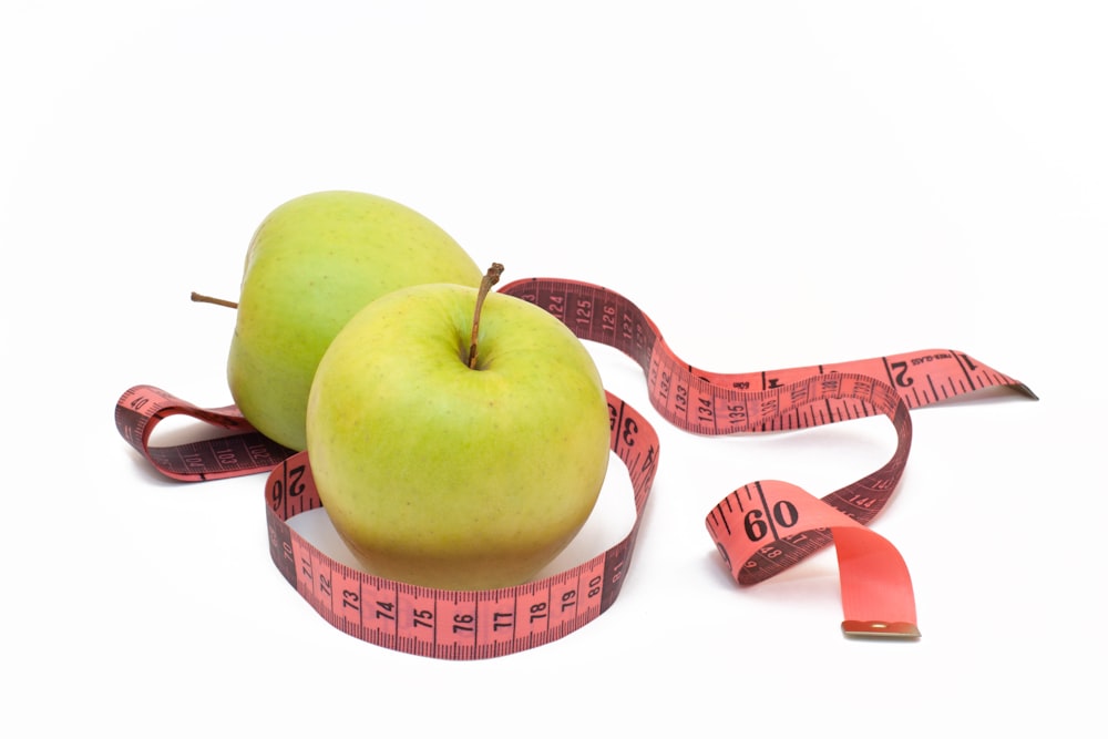 two green apples with a measuring tape around them