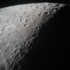 A detailed view of the moon's surface showcasing numerous craters and rugged terrain, with a strong contrast between illuminated and shadowed areas.