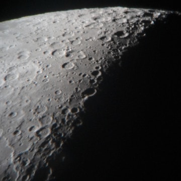 A detailed view of the moon's surface showcasing numerous craters and rugged terrain, with a strong contrast between illuminated and shadowed areas.