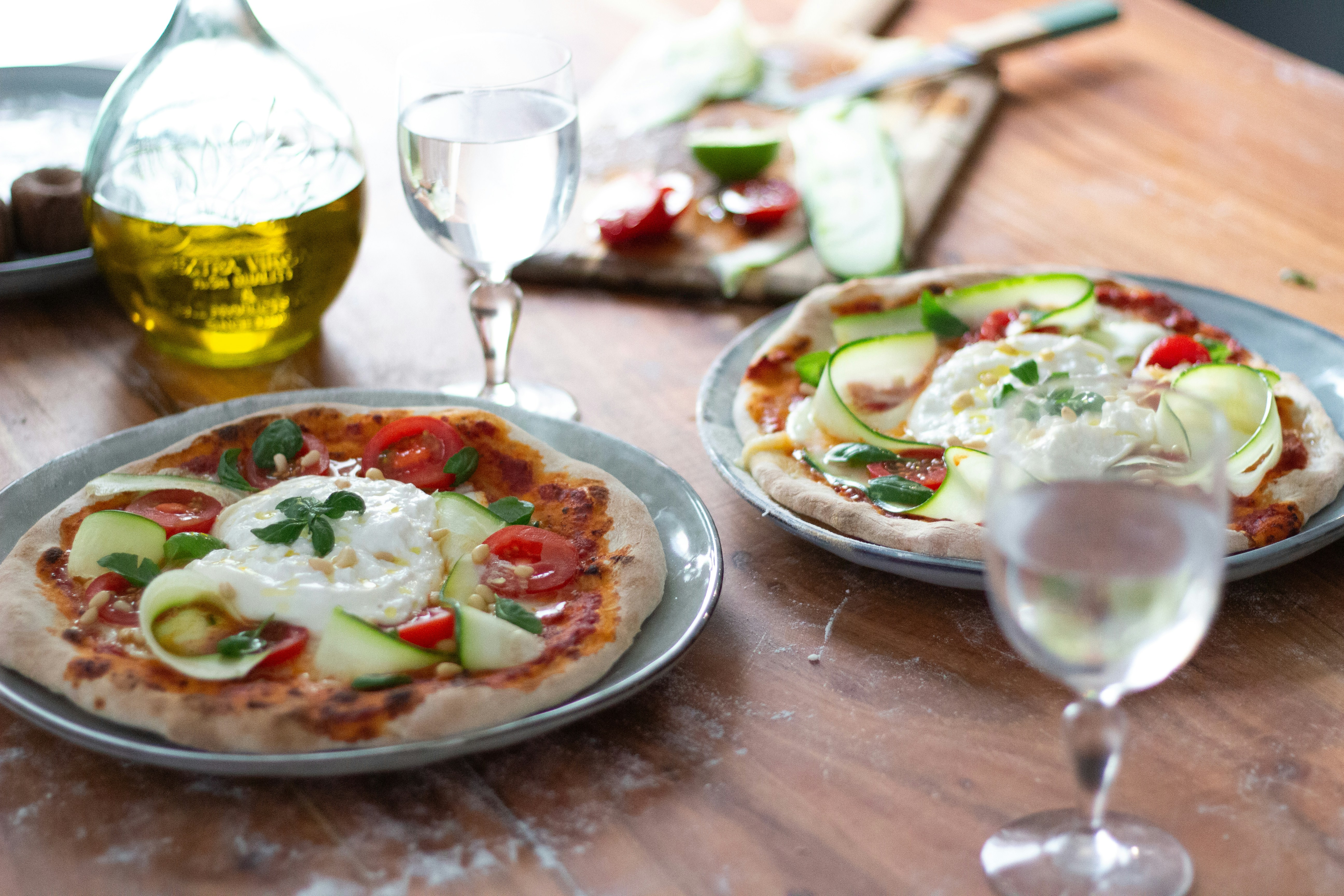 a wooden table topped with two pizzas and glasses of wine