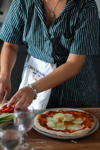 a woman cutting up a pizza on top of a wooden table