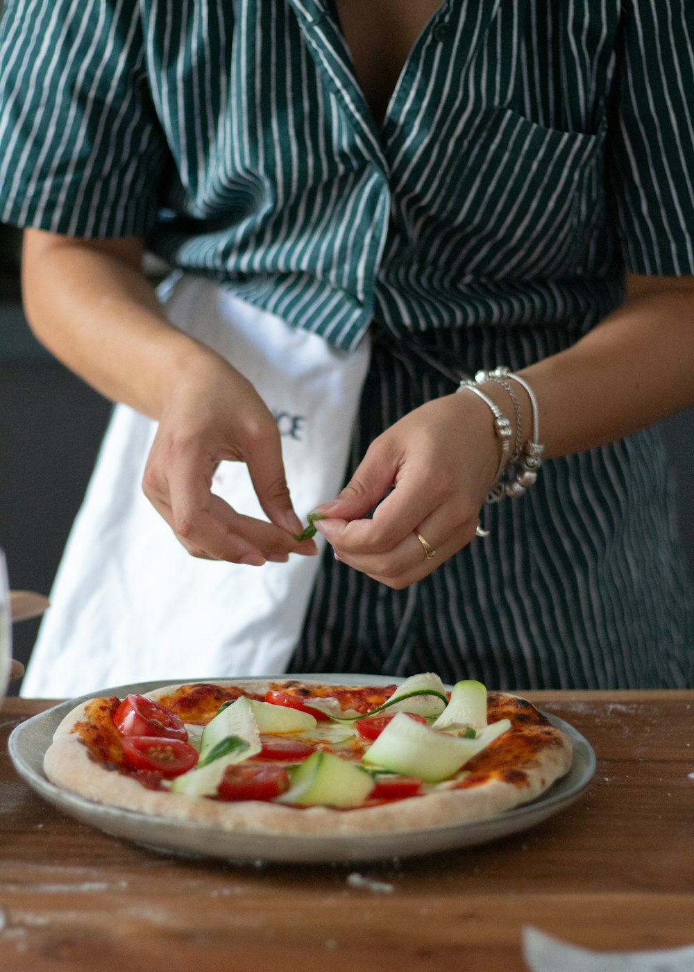 a woman preparing a pizza on top of a wooden table