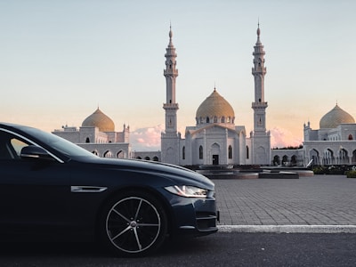 A sleek navy Toyota Camry parked outside a mosque at sunset, bathed in golden light.