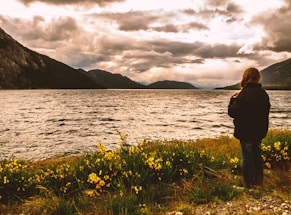 a person standing near a body of water with mountains in the background