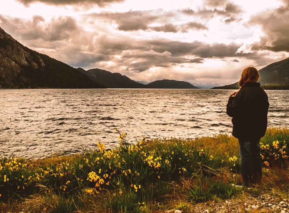 a person standing near a body of water with mountains in the background