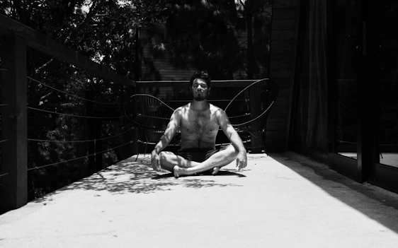 Rajeswer Naidu sitting peacefully in a serene outdoor setting, meditating with gentle sunlight filtering through trees.