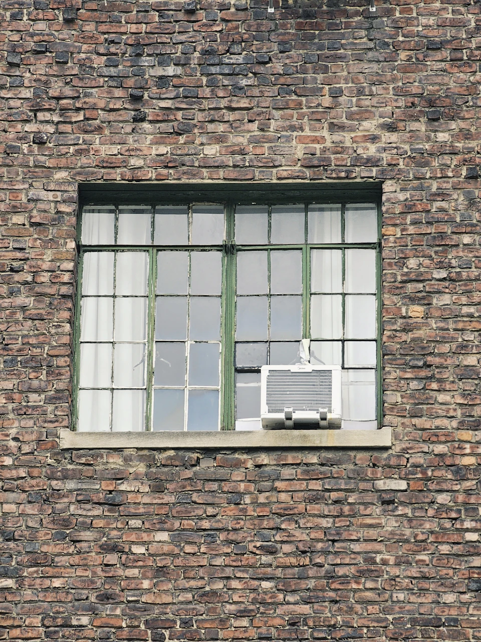 Closed window with green bars and white curtains on a brick wall exterior