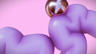 A surreal image featuring two purple, inflated, abstract shapes against a pink background. A shiny, metallic, spherical object with reflective properties is situated at the top of one of the shapes.