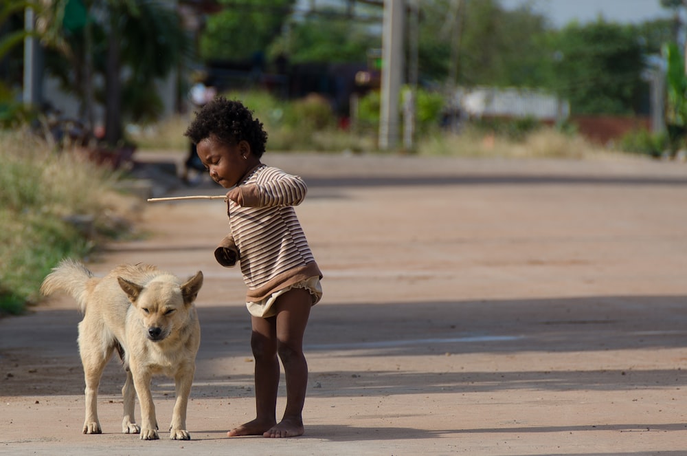 a little girl standing next to a dog on a dirt road