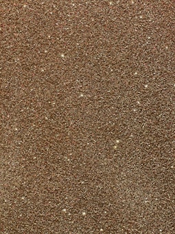 A textured surface densely covered in gold glitter particles that create a shimmering effect as they catch the light, presenting a glamorous and luxurious appearance.