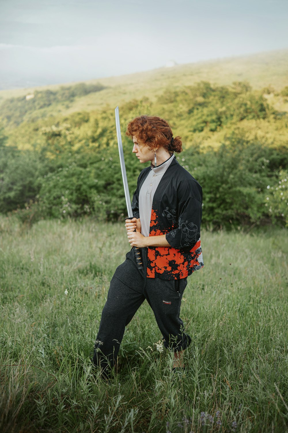 a woman with red hair holding a sword in a field