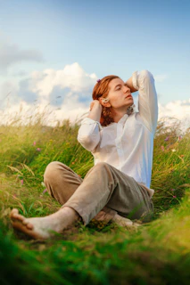 a woman sitting in the grass with her hands on her head