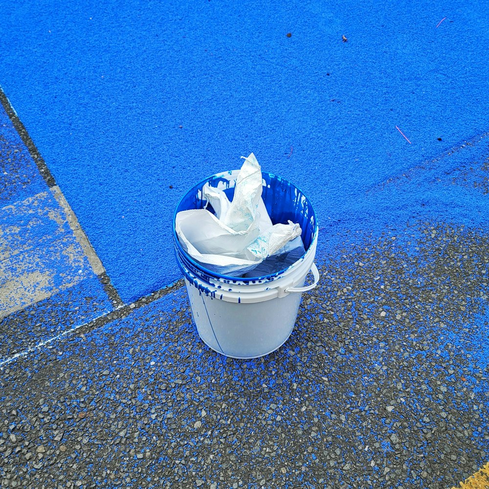 a blue and white trash can sitting on the side of a road