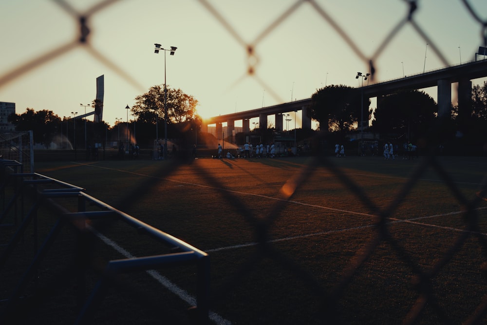 the sun is setting behind a chain link fence