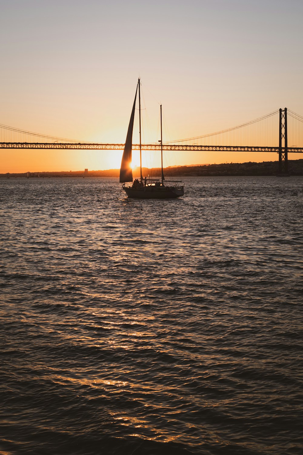 a sailboat in the water with a bridge in the background